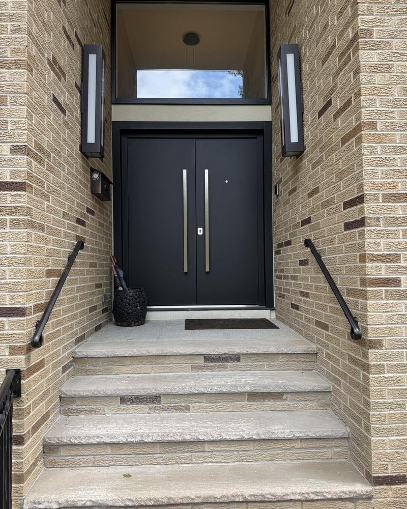 Double entry door with full-height pulls and a glass transom, set into a brick entry