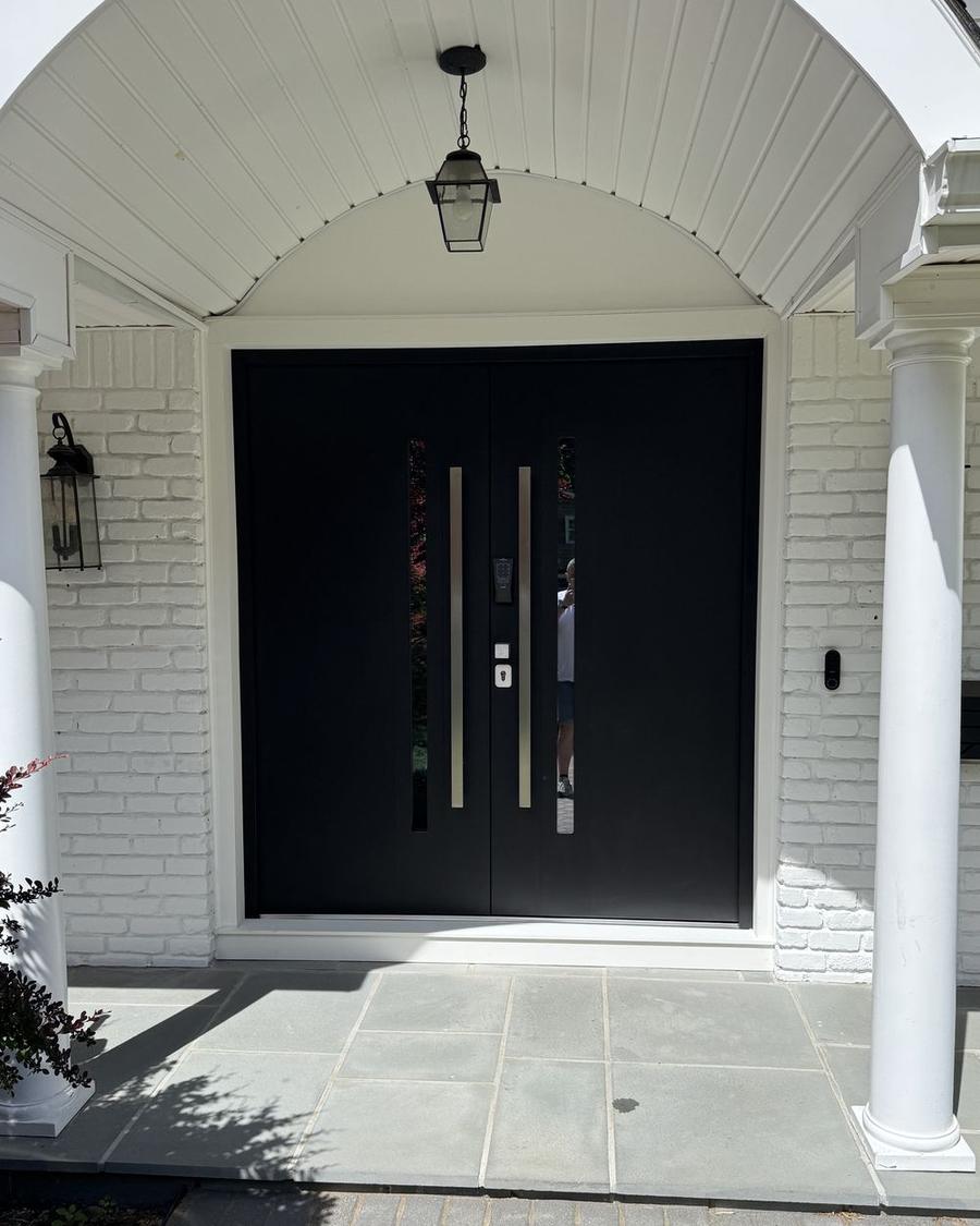 Black double entry door under an arched portico on a white brick house