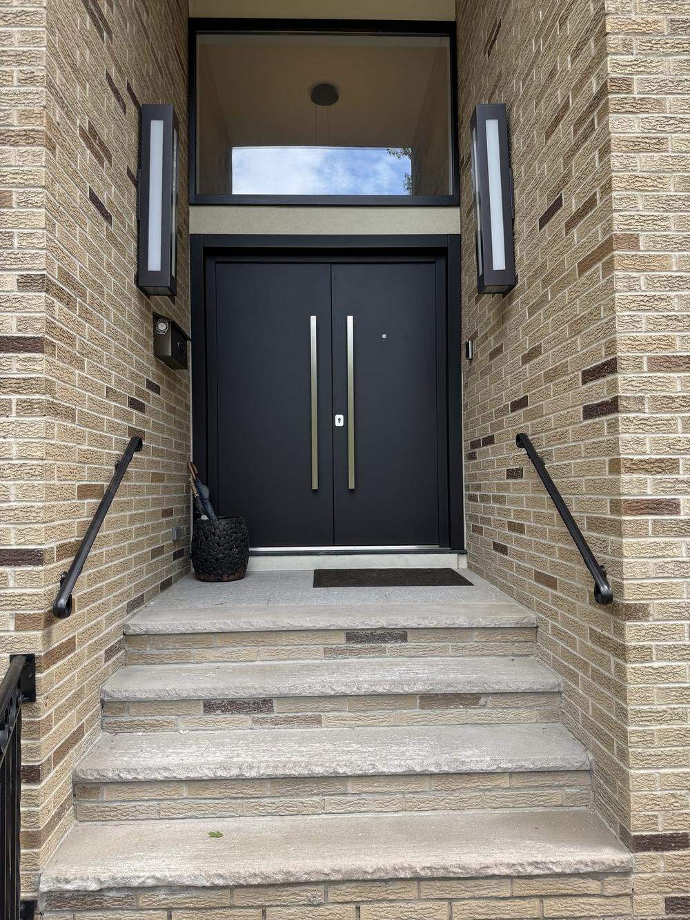 Black double entry door with full-height stainless pulls, installed in a brick entryway with stone steps